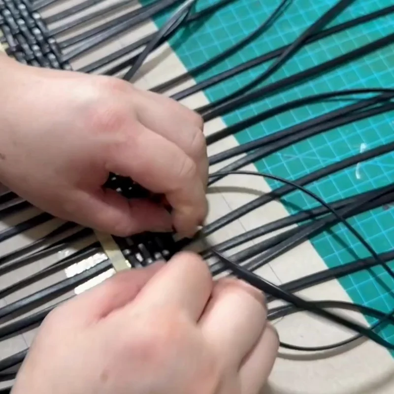 Close-up of hands weaving strips on a work surface
