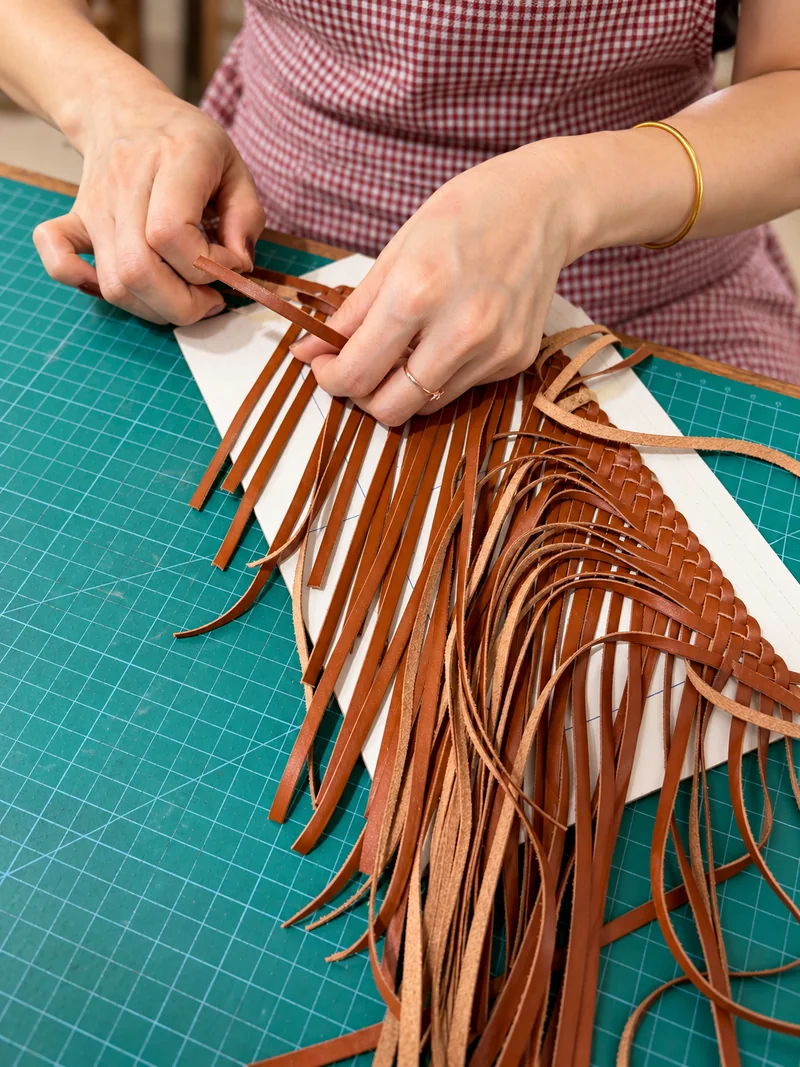 Hands weaving leather strips for bag construction at TruGrain