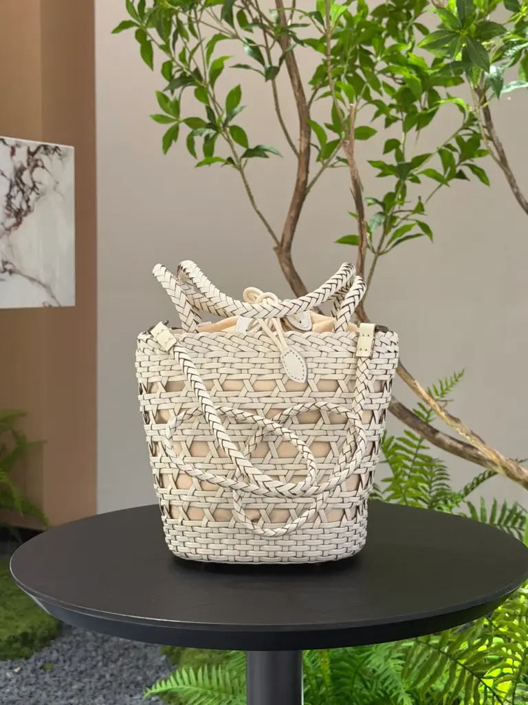 Cream woven leather bucket bag with an open-weave body, two handles, a detachable long shoulder strap and fixed fabric lining